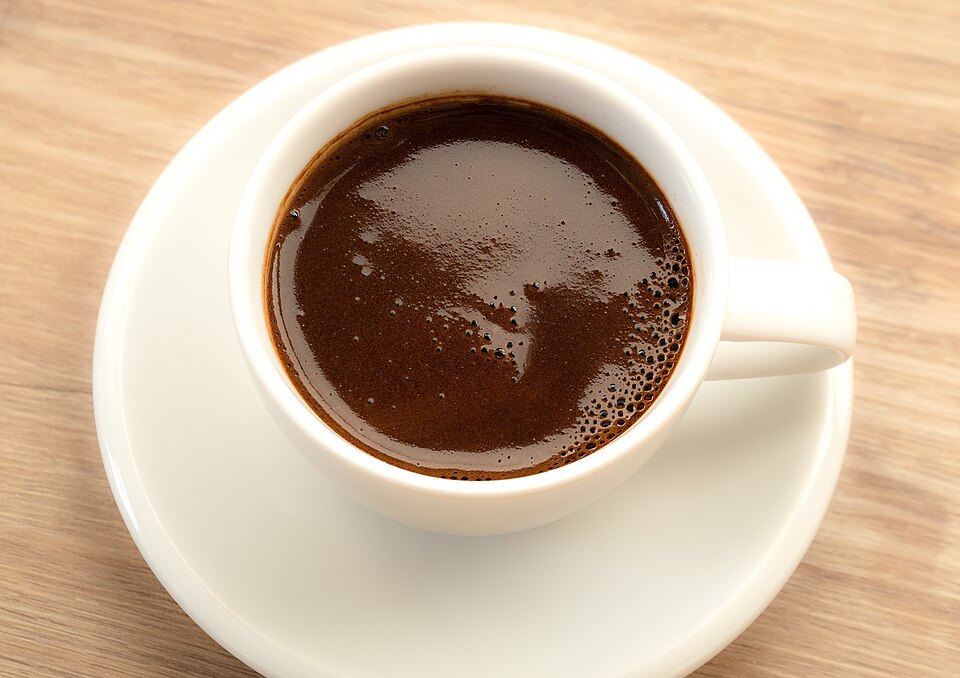 Black coffee in a white ceramic cup and saucer on a wooden table